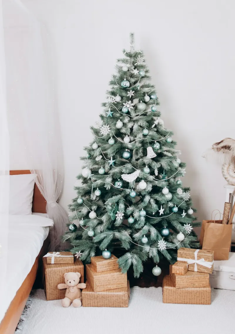 Sapin de Noël décoré, avec des cadeaux emballés et un ourson en peluche à son pied